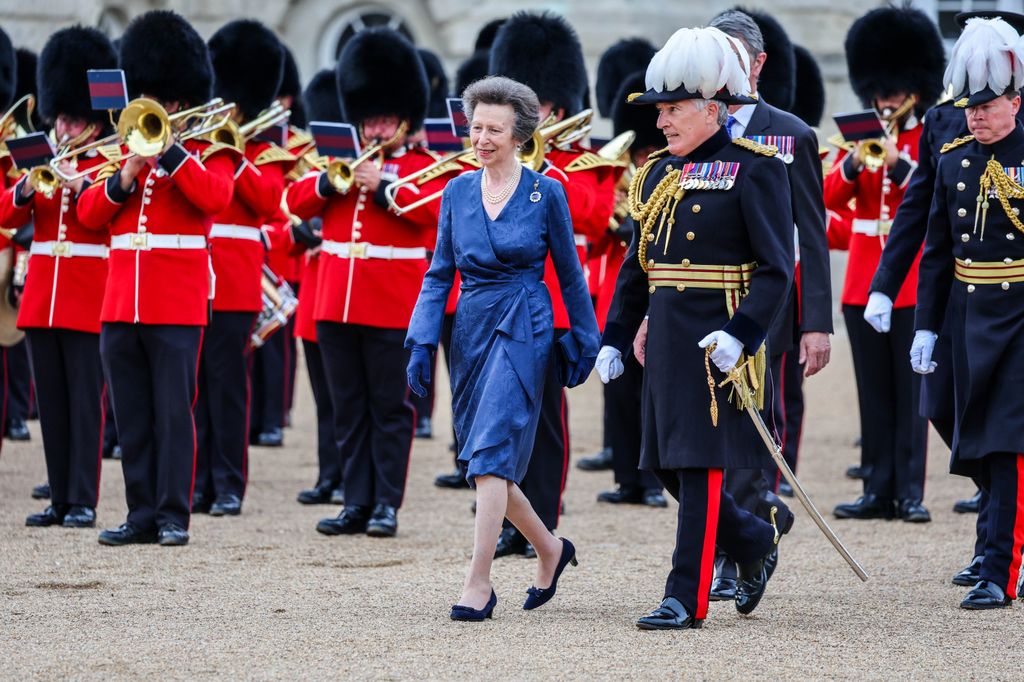 Princess Anne and Major General James Maurice walking through crowd of beefeaters playing trumpets