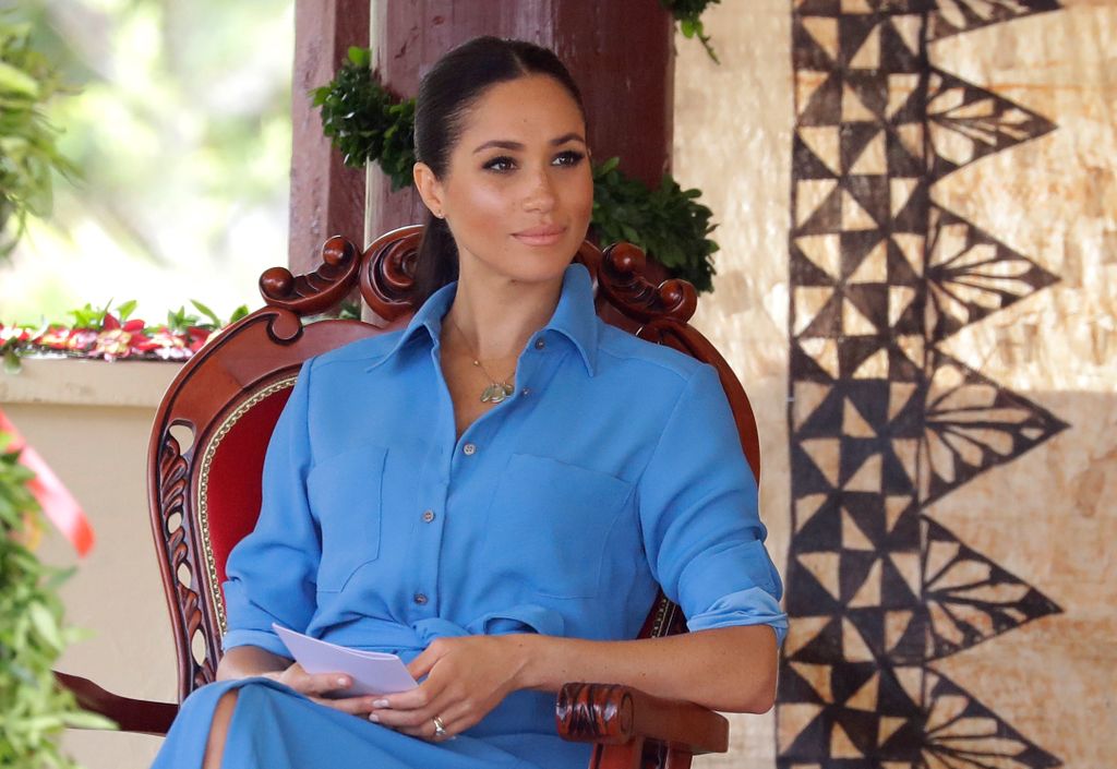 Meghan Markle wearing a blue dress and holding paper