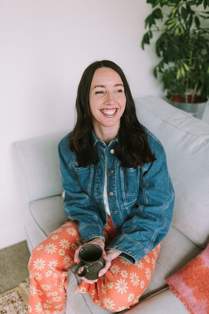 woman wearing bright trousers and a denim jacket holding a hot drink