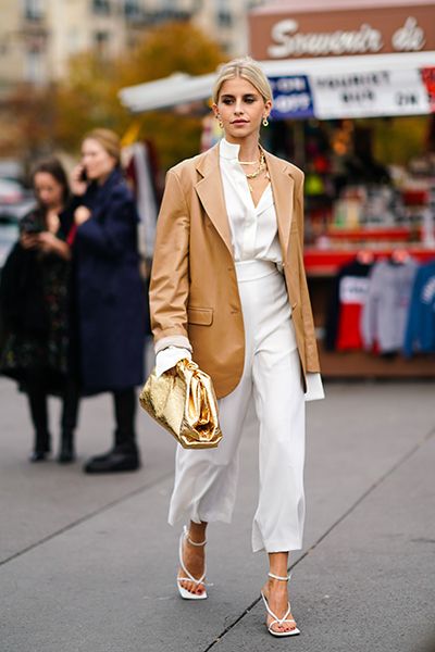 Woman wears camel blazer and white trousers