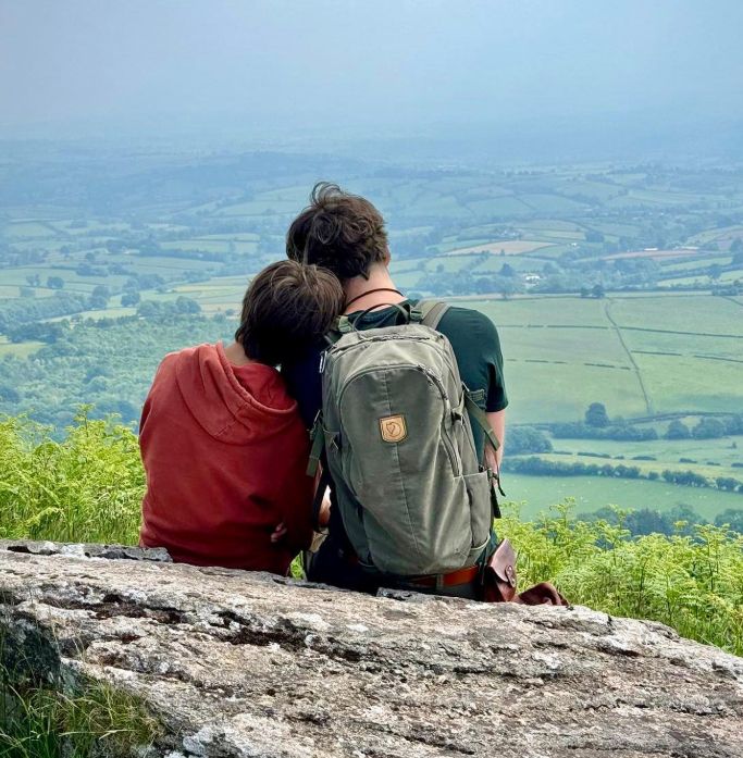 Simon Reeve and his son resting their heads on one another while sitting on a hill