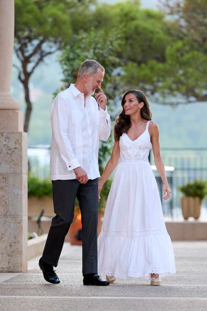 King Felipe and Queen Letizia smiling at eachother outside in white