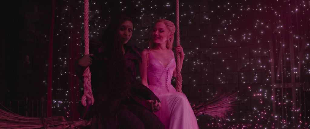 A photo of Ariana Grande and Cynthia Erivo holding hands on a broomstick