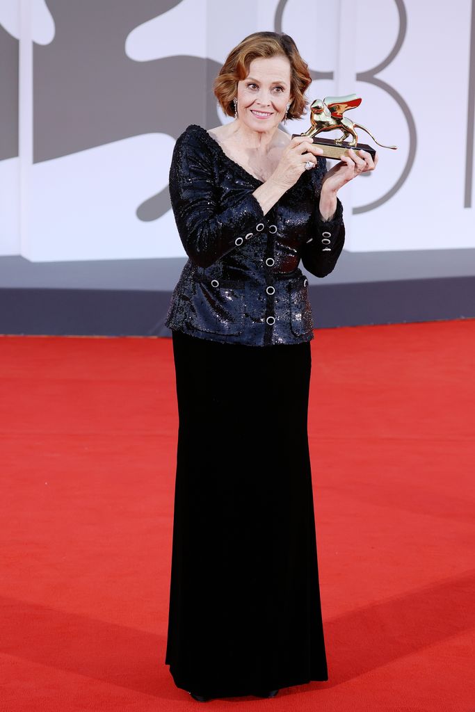 Sigourney Weaver holding a golden lion in an all-black outfit