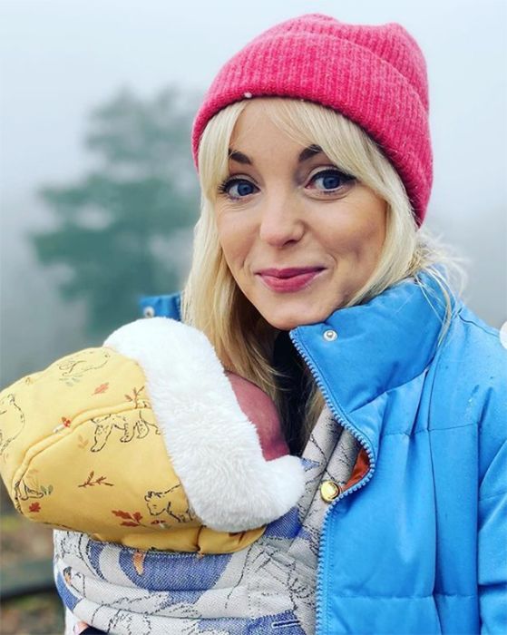 Helen George wears red hat with baby in sling