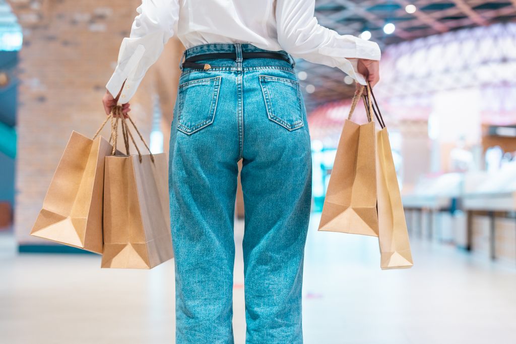 Back view of a woman wearing jeans in a city mall with shopping bags.