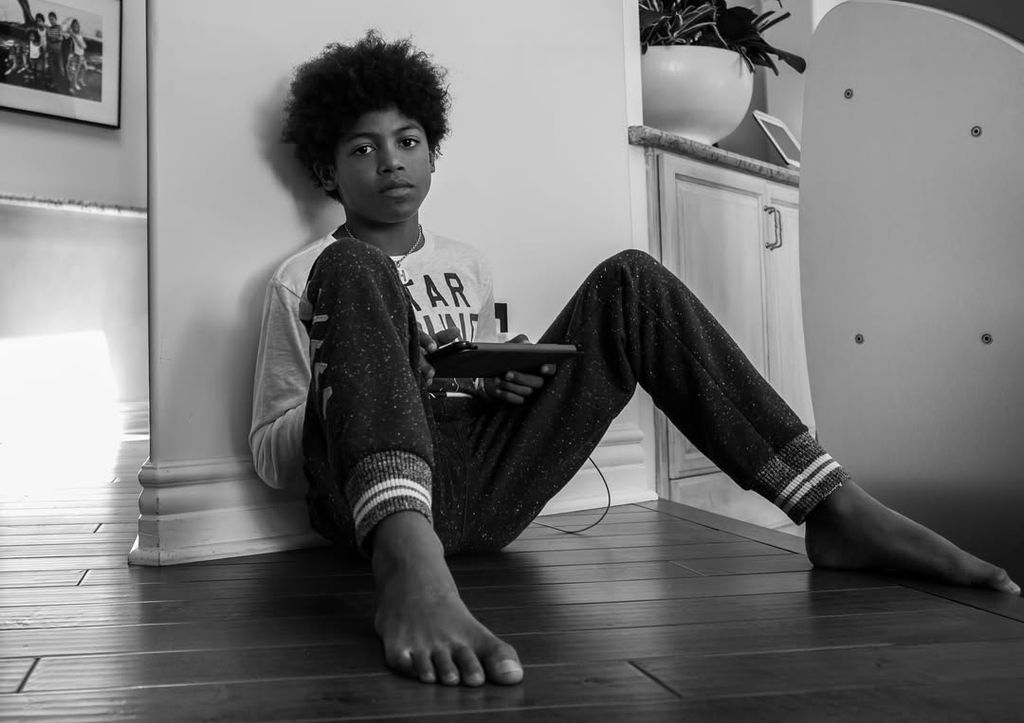 Black and white photo of Henry Samuel sat on floor on phone posing for the camera
