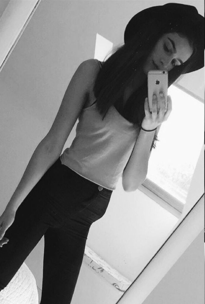Brunette girl in a tank top and skinny jeans taking a selfie 