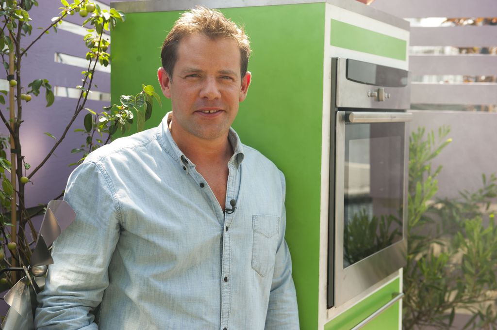 Matt Tebbutt in a blue shirt standing with a green kitchen unit