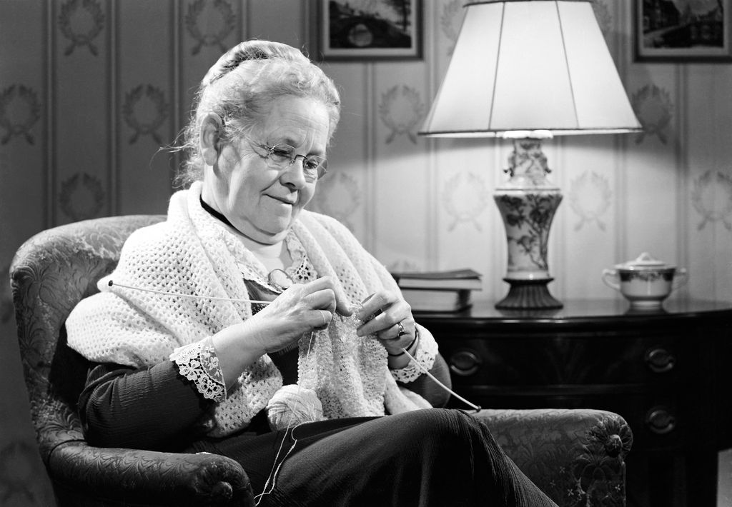 Old lady knitting in an armchair with a shawl around her 