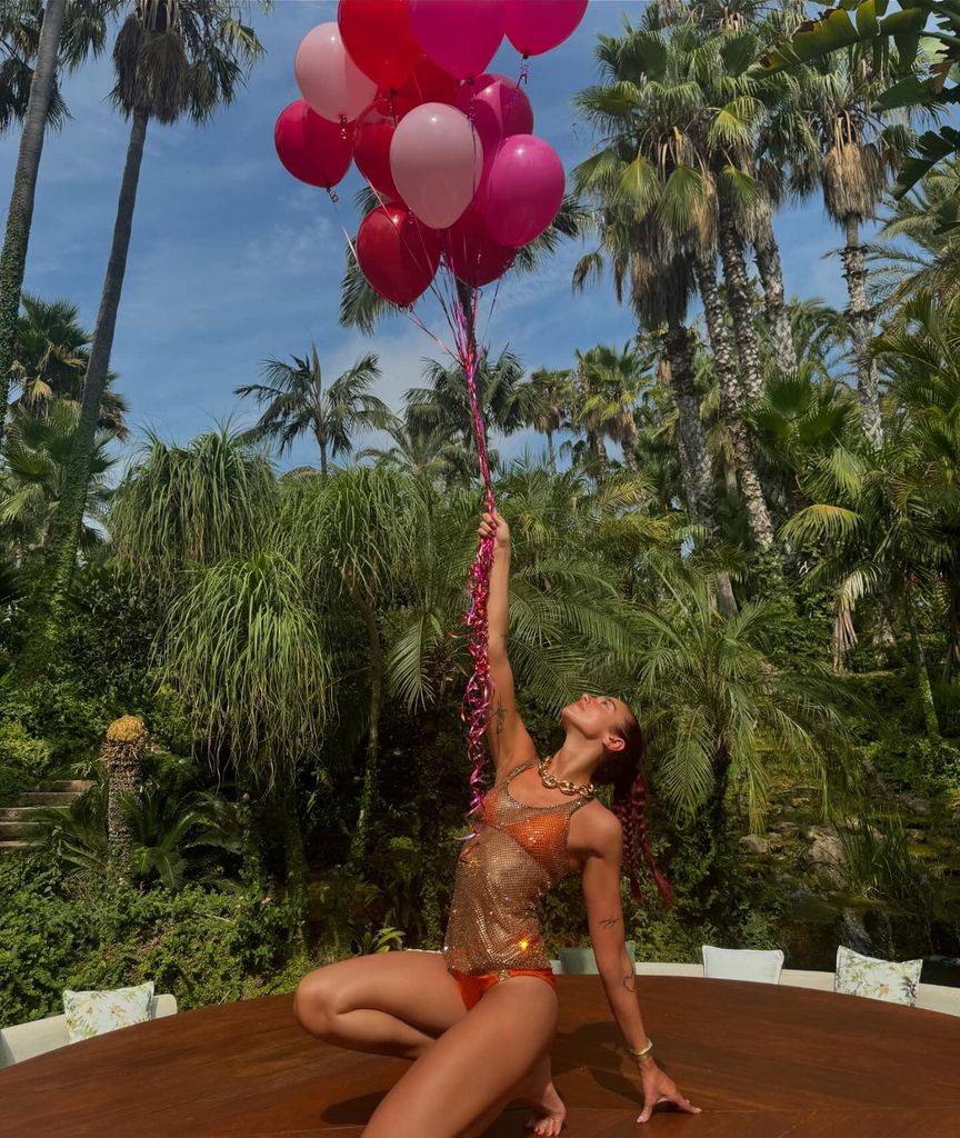 Dua posed in orange bikini on table holding balloons