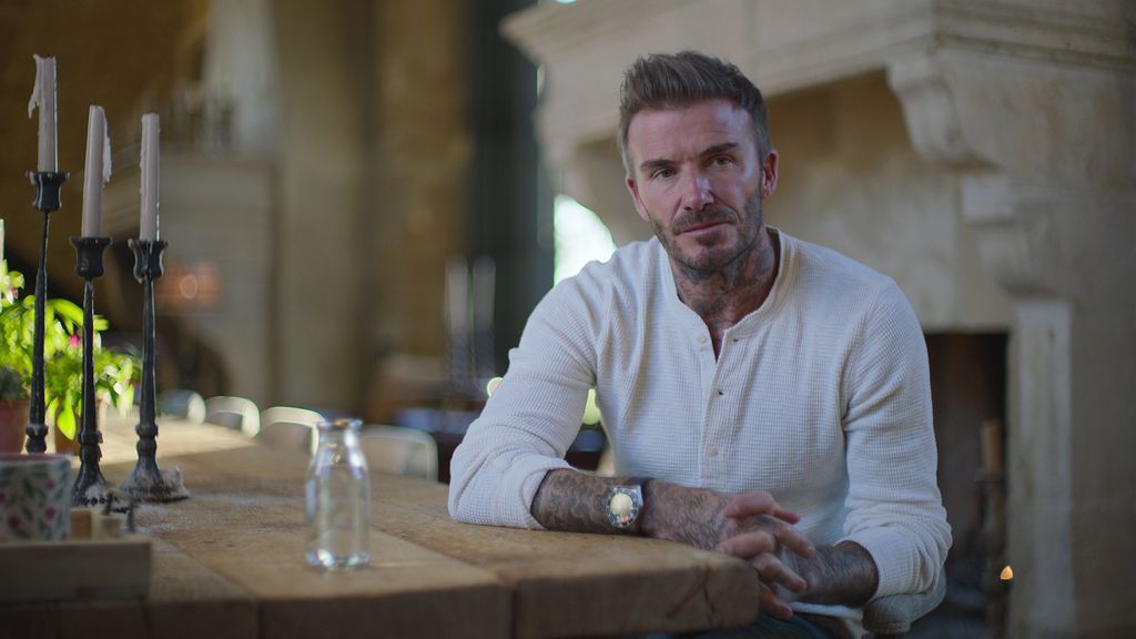 David Beckham sat at wooden table in white jumper
