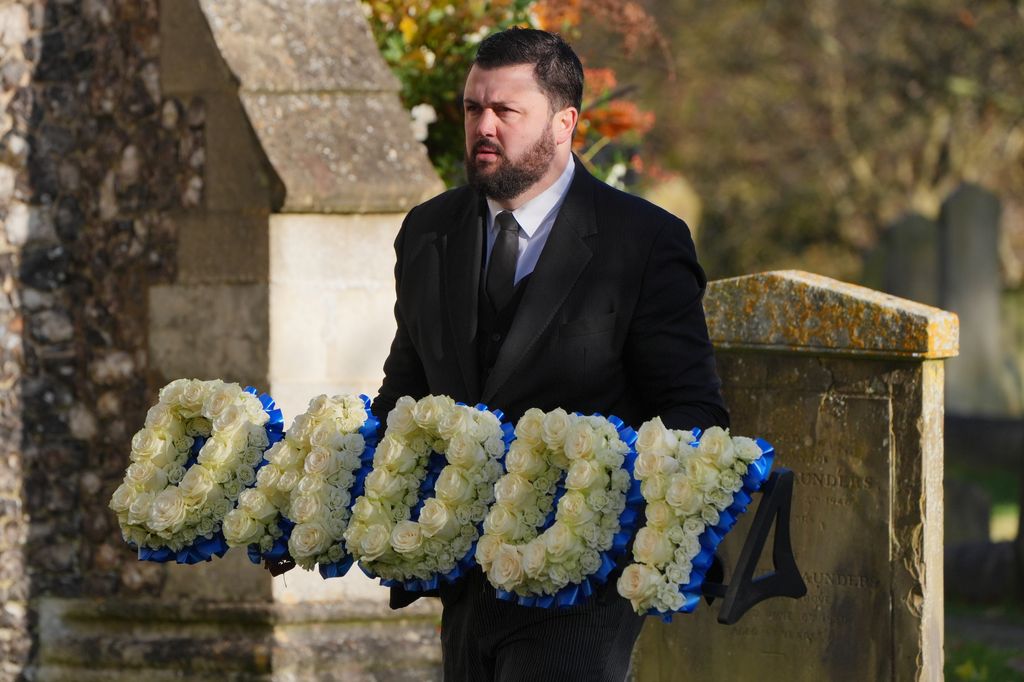 A funeral director carries the floral tribute