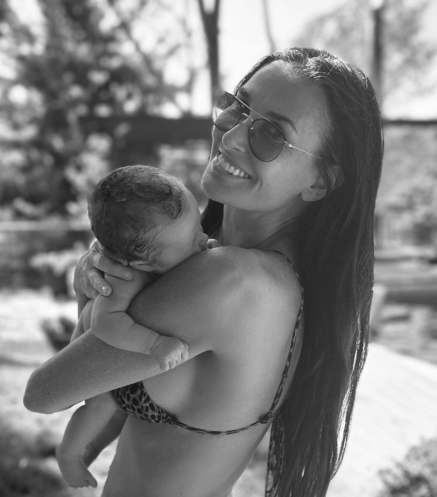 Demi holds her newborn granddaughter Louetta while wearing a bikini