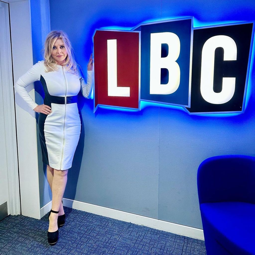 Carol Vorderman in a white dress next to an LBC sign