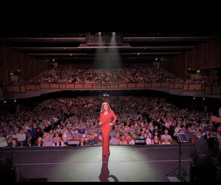 Jane McDonald in a red outfit in front of a crowd of people