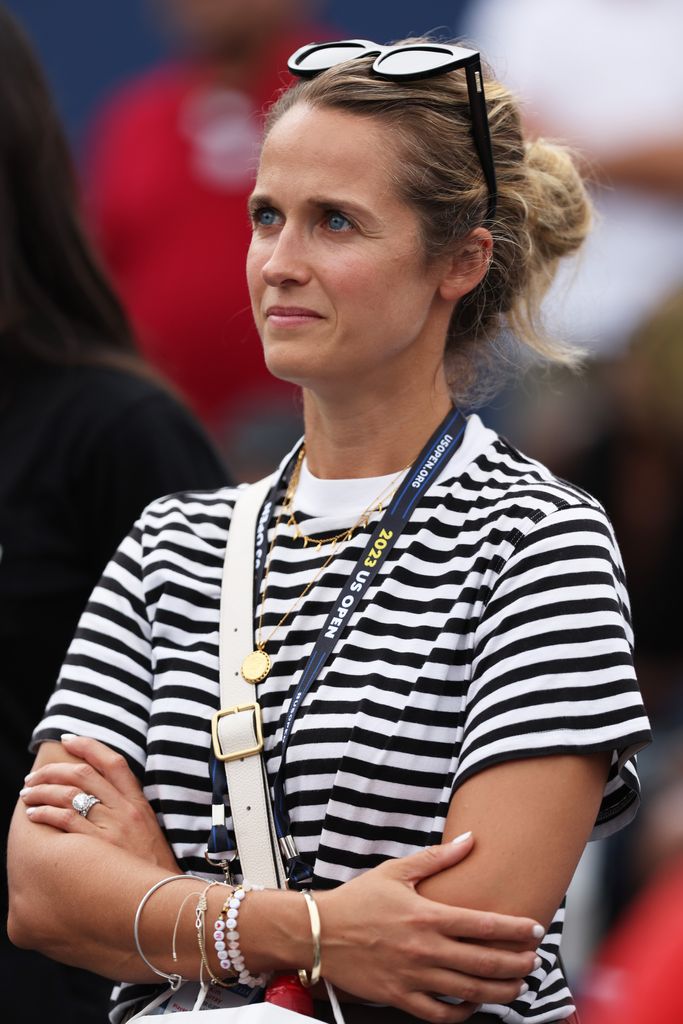 Kim Murray in a striped T-shirt with her hair in a bun watching her husband play tennis