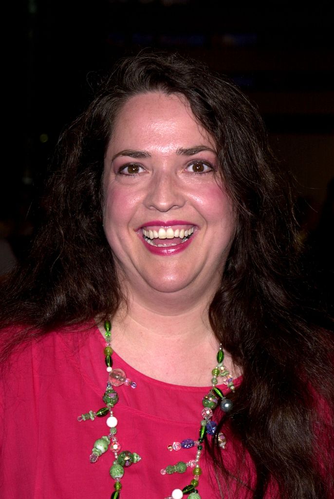 Anya Kubrick sourit dans une robe rose vif et un collier de perles vertes.