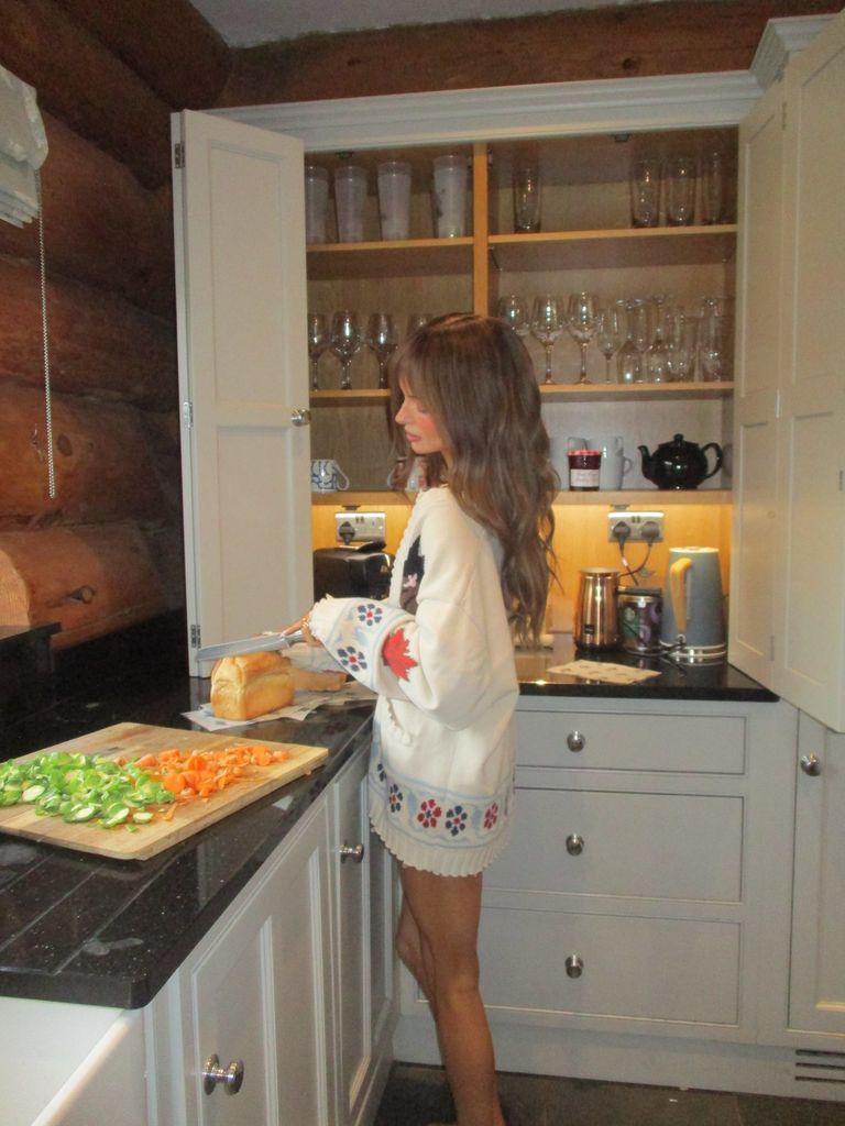 Maura Higgins wears an oversize jumper and stands in a kitchen cutting a loaf of bread