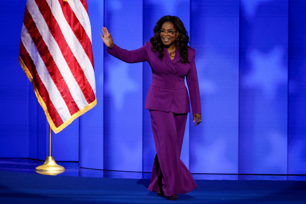 Oprah Winfrey no palco acenando em um terno roxo poderoso