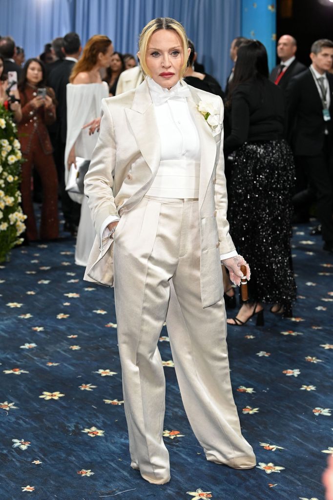 Madonna wears a cream satin suit with white shirt and white mesh lace gloves. She is holding a cigarette.