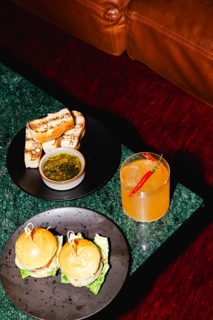 A cocktail, some bread and dips, two mini burgers and an orange cocktail with a chilli on top