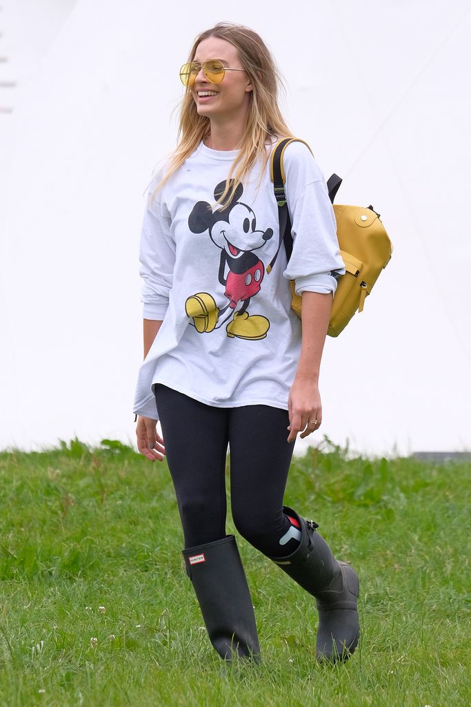 Margot Robbie attends day two of Glastonbury on June 24, 2017 wearing black leggings, a Mickey Mouse shirt and yellow sunglasses.