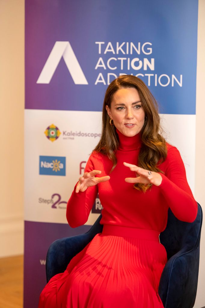 Kate Middleton in a red dress in front of a charity banner