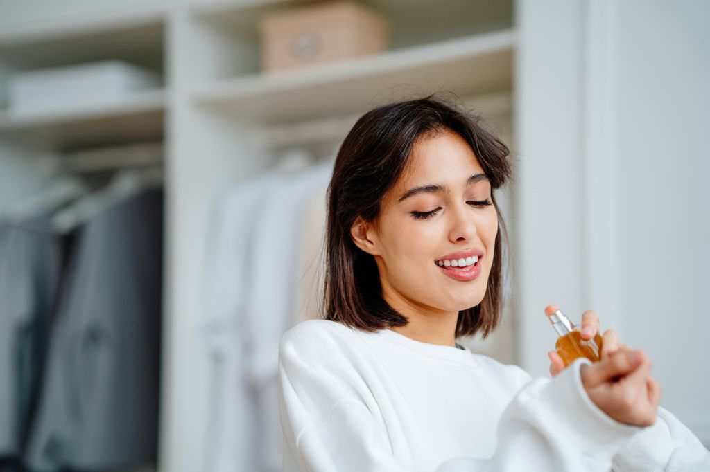 Seductive, satisfied brunette woman applying spraying perfume bottle as essential oil on the wrist
