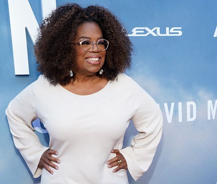 Oprah Winfrey has her hands on her hips as she wears white dress