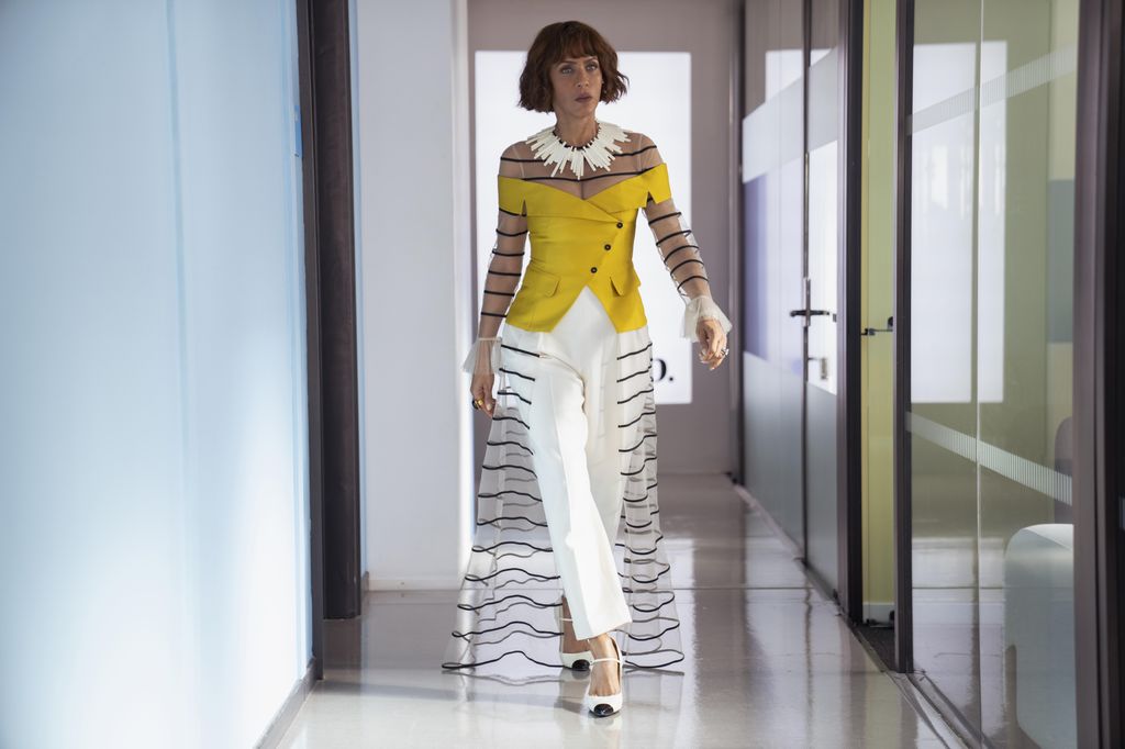 Lisa wearing a black striped sheer cape over a pair of white trousers and a yellow bardot corset on And Just Like That