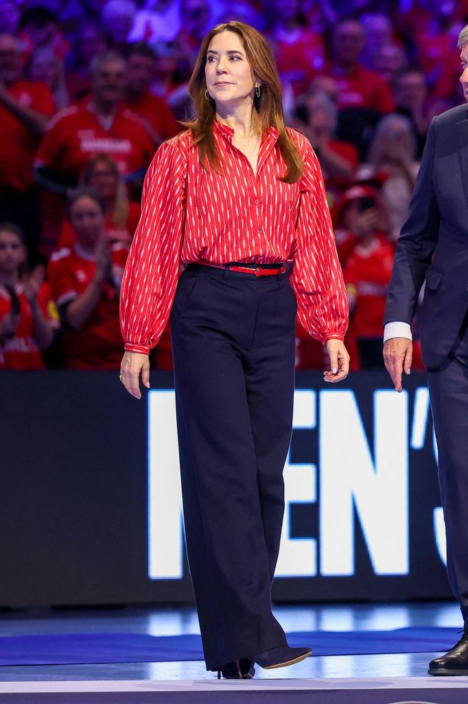 Queen Mary sur un terrain de handball en chemise rouge et pantalon bleu marine