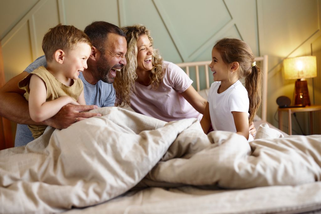 Cheerful parents having fun with their small kids during morning time on a bed in bedroom.
