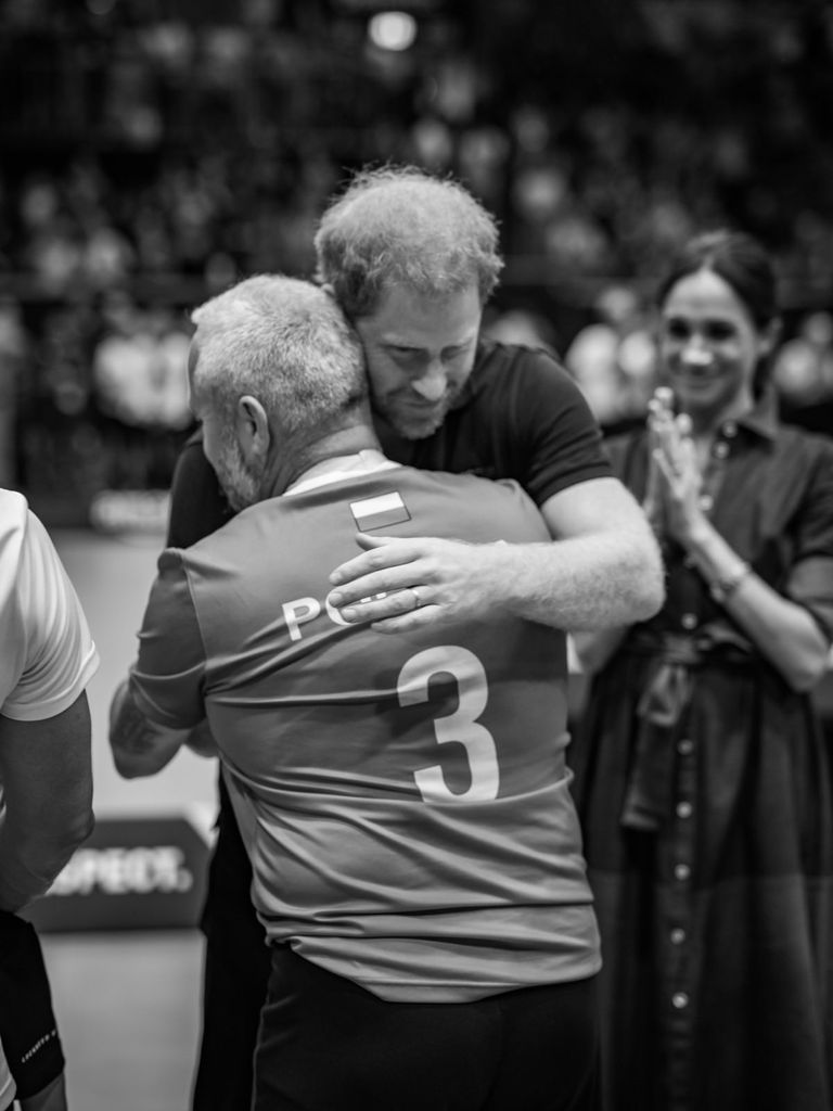 Prince Harry is watched by Meghan Markle as he hugs an Invictus Games competitor