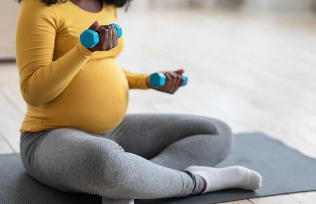 Pregnant woman in a yellow top and green leggings exercising with dumbbells