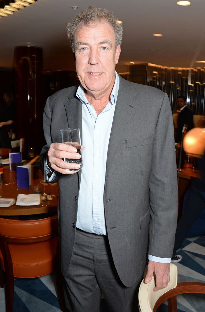 Jeremy Clarkson holding a glass of water in a grey suit