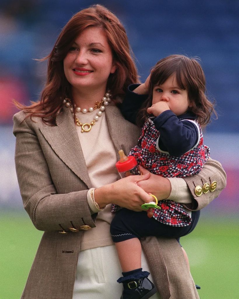 Karren Brady carrying her young daughter on a football pitch