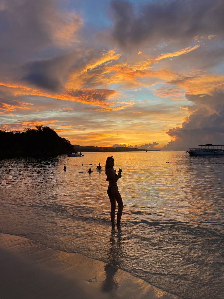 A woman standing on Beach with an orange and blue sunset behind