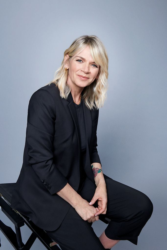 Zoe Ball sitting in a black suit with a grey background