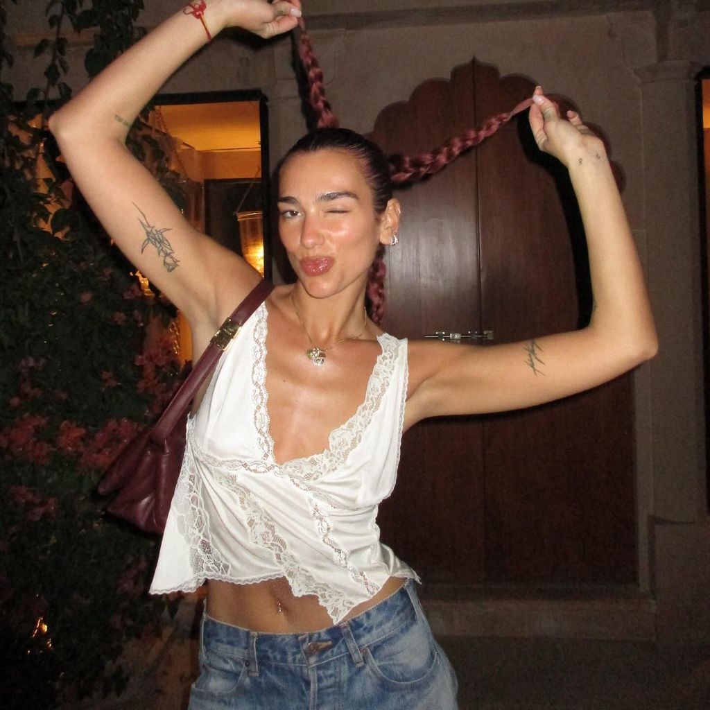 Dua holding her braided hair up in white crop and jeans