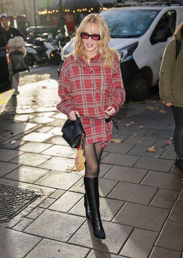 Kylie Minogue in a tartan dress, knee-high black boots and a black bag with a gingerbread man charm
