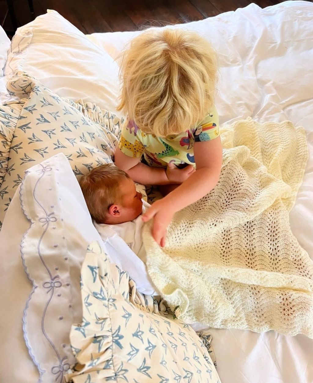 A blonde child putting a blanket over a baby