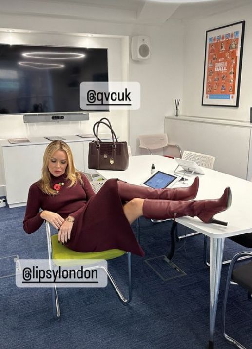 Amanda Holden lounging on a chair and desk in burgundy dress and boots