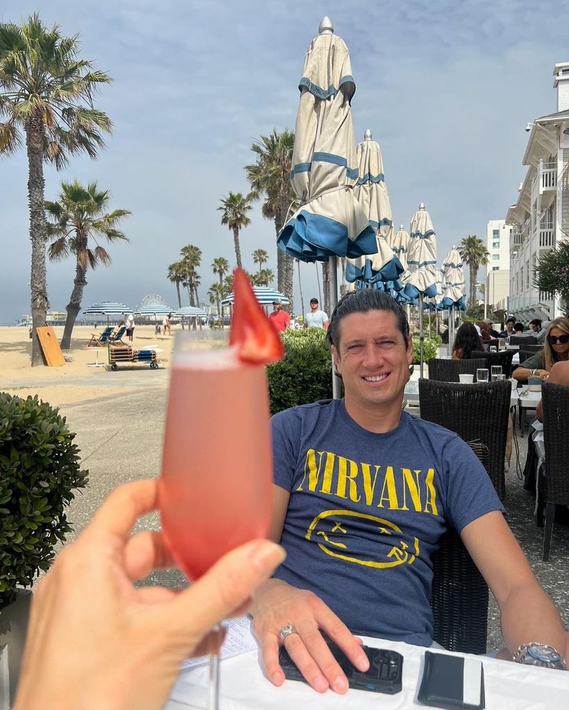 Vernon Kay smiling while Tess holds up pink drink on beach