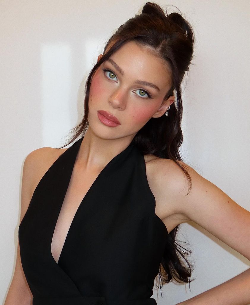 Nicola Peltz wearing a black halterneck top with her hair half-up half-down and a make up look featuring romantic rosy cheeks
