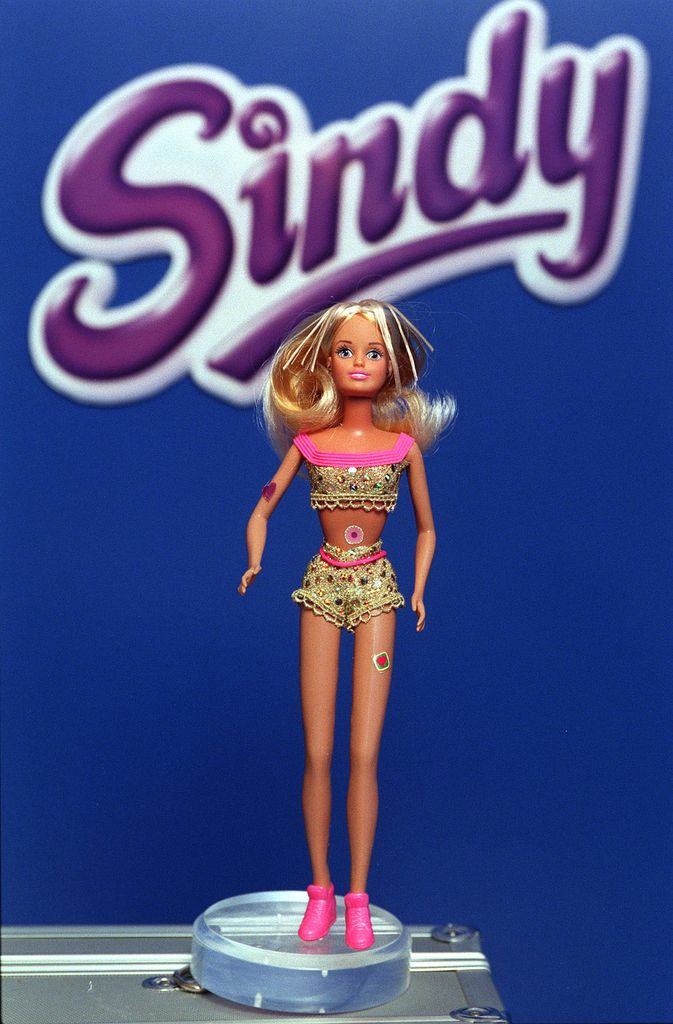 Une poupée se tient sur une petite plate-forme avec une pancarte indiquant Sindy derrière elle.