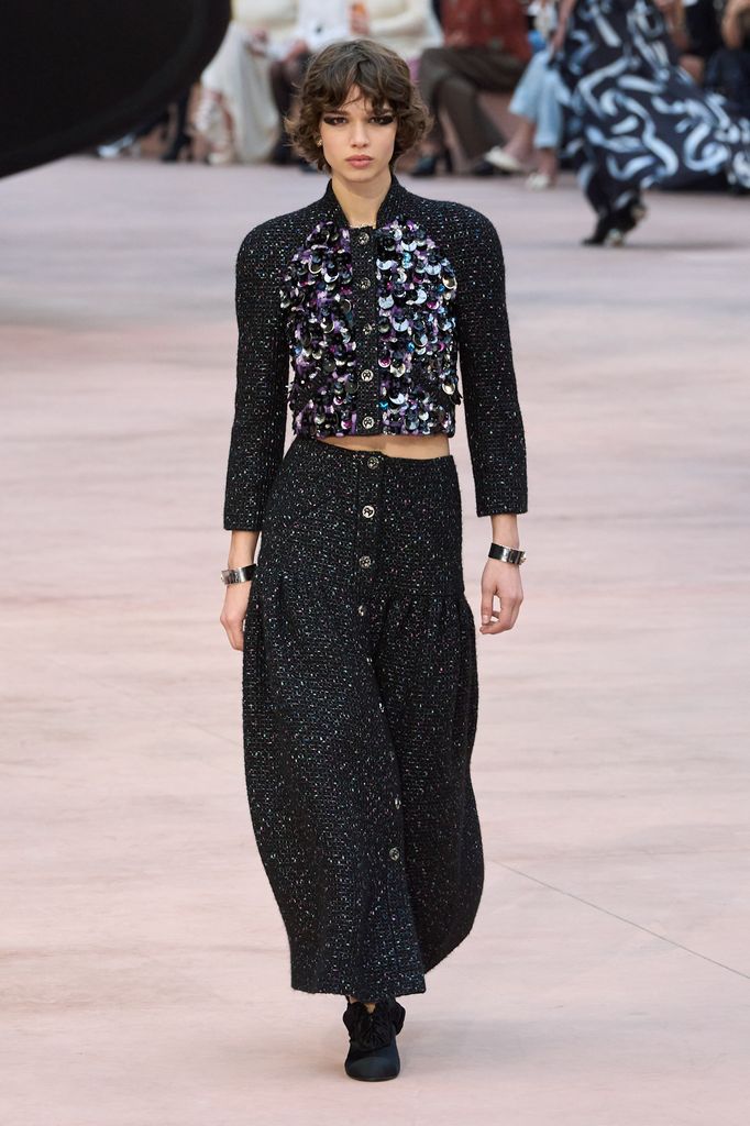 A model walks the runway at Chanel wearing a sequinned jacket and long black lurex skirt. 