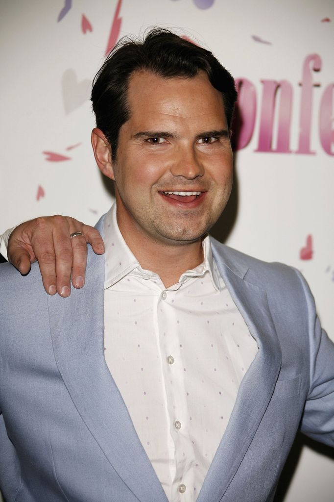 Jimmy Carr smiles as he extens his arm out to the side while posing with fellow celebrities on the red carpet