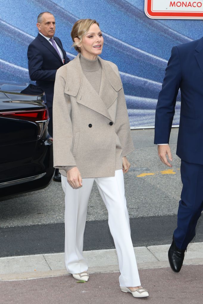 Princess Charlene walking in white trousers and taupe coat