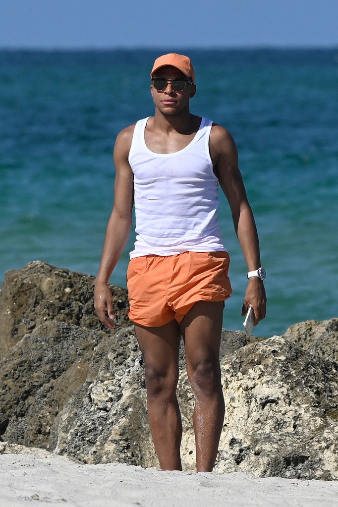 Kylian Mbappe in orange swim trunks on the beach